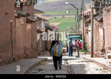 Una Donna Peruviana con un colorato back pack cammina giù per una strada nella città di Maras nella Valle Sacra degli Incas del Perù. Foto Stock