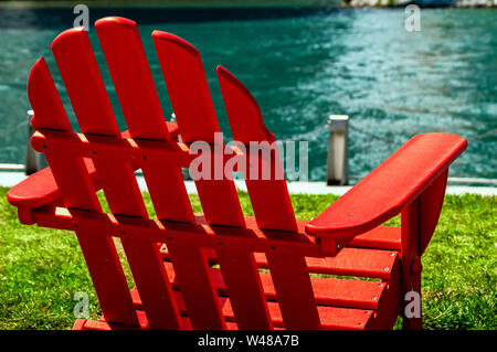 Un rosso di legno sedia prato sul lungomare riverwalk in una giornata di sole. Scena all'aperto. Foto Stock