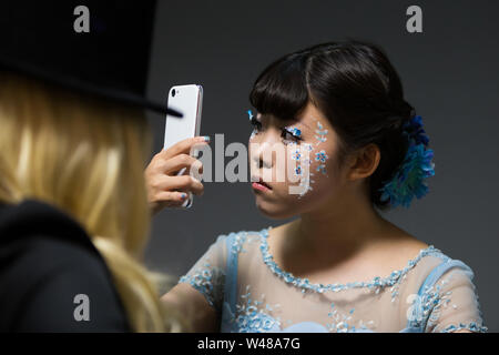 Chiba, Giappone, 02/18/2019 , Giapponese giovane modello con facepaint preparando per scattare una foto guardando il suo telefono cellulare. Foto Stock