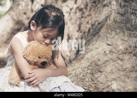 Ragazza triste sensazione da sola nel parco. Lonely concetti. Bella ragazza per bimbi più grandi e soffici rimanere solo sotto il grande albero. Foto Stock