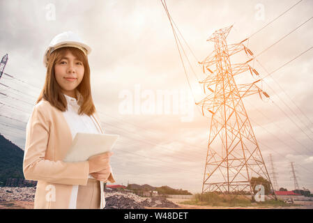 Smart giovane bella ingegnere elettrico donna che lavorano utilizzando tablet per controllare le reti di alimentazione elettrica alla fabbrica. Foto Stock