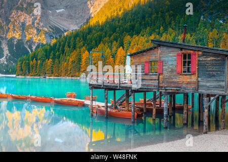 Il pittoresco lago alpino e il bellissimo paesaggio autunnale con giallo larici. Popolare destinazione turistica con barche di legno e legno carino boathouse, Foto Stock