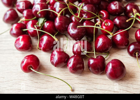 Mature succose bacche rosse di ciliegio dolce sono casualmente disperse su una luce tavolo in legno Foto Stock