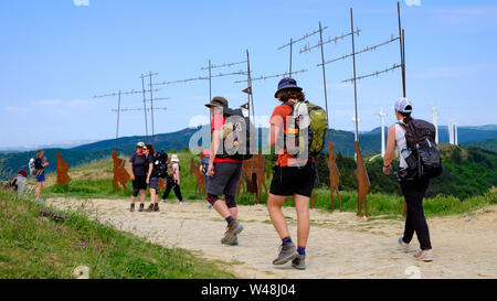 Pellegrini camminando sul Camino de Santiago. Walkers arrivando al monumento alla sommità dell'Alto del Jordon, mentre altri prendere le foto sul loro break Foto Stock