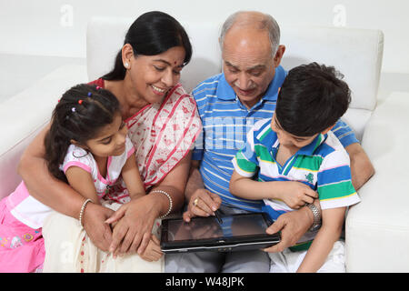 Indian vecchia coppia con i loro nipoti utilizzando una tavoletta digitale Foto Stock