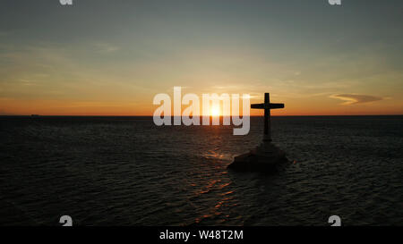 Croce cattolica nel cimitero affondata nel mare al tramonto, Vista aerea. Colorato nubi luminose durante il tramonto sul mare. Tramonto al cimitero affondata Camiguin Island Filippine. Foto Stock