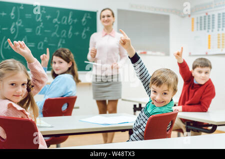Gli studenti nella classe alzando le mani per rispondere a una domanda Foto Stock