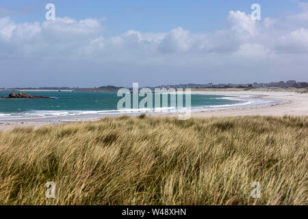 Kitesurfisti e windsurf con i loro aquiloni e surf cavalcare le onde con nubi nel cielo a lunga spiaggia sabbiosa in Bretagna, Francia Foto Stock