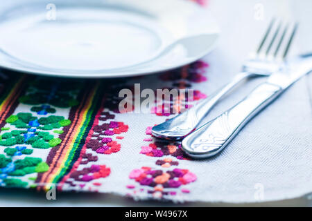 Impostazione tabella per la cena: una piastra bianca, una forchetta, un coltello su un tessuto assorbente con un disegno ricamato, tradizionale a mano in Ucraina Foto Stock