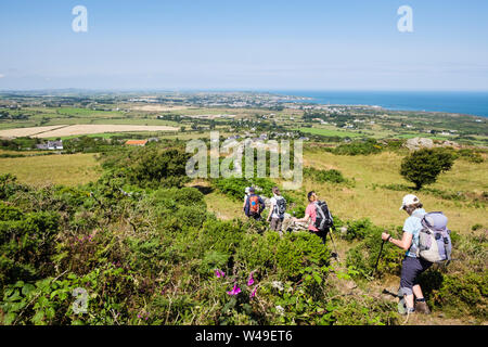 Gli escursionisti escursioni a piedi giù per un sentiero sulla Mynydd Eilian con vista Amlwch sulla costa. Llaneilian, Isola di Anglesey, Galles del Nord, Regno Unito, Gran Bretagna Foto Stock