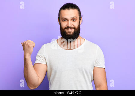 Cheeful sorridente barba lunga man looking e rivolta verso il lato con il pollice fino.close up verticale. Il linguaggio del corpo, direzione guarda qui. In questo modo, si prega di Foto Stock