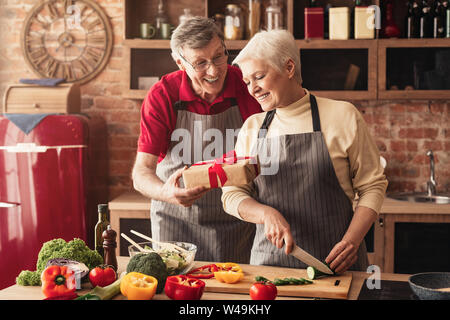 Cura Uomo senior dando confezione regalo per sua moglie in cucina Foto Stock