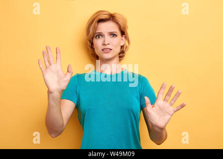Nervoso gravi donna bionda mostra le palme nella fotocamera isolate su sfondo giallo. fobia , paura , emozioni e sensazioni Foto Stock