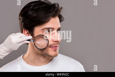 Il dermatologo guardando al giovane la pelle del viso attraverso la lente di ingrandimento Foto Stock