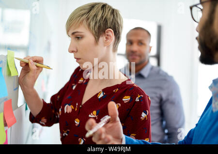 Ritratto di una bionda di capelli corti donna a capo di un team diversificato di creative millenaria i colleghi in un avvio di proporre idee Foto Stock