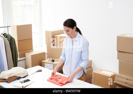 Giovane donna online shop lavoratore piegatura maglione rosso per il confezionamento Foto Stock