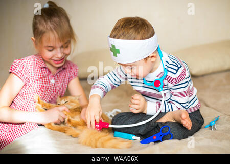 Little Boy in bicchieri con la sindrome di Dawn e ragazza bionda giocare con giocattoli e ginger cat. Foto Stock