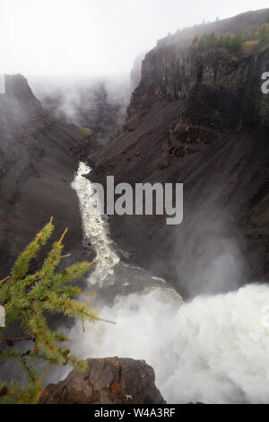 La maestosa cascata che si tuffa nel Rugged Canyon circondato da montagne innevate nell'altopiano di Putorana, a nord della Russia, riserva naturale di Putoranskiy. Foto Stock