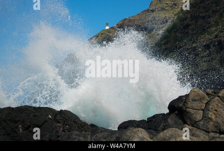 Vista di un onda di schiantarsi contro una costa rocciosa con il faro Mokapu in background. Questo è su Oahu, Hawaii's south shore. Foto Stock