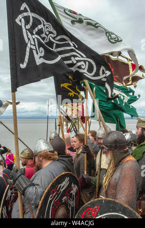 Età vichinga, costumi di abbigliamento e armi a Heysham, Lancashire. Luglio, 2019. Le bandiere di battaglia volano alla baia di Morecambe mentre 70 re-enactors del guerriero di eredità storica si riuniscono ad un'accampamento di storia vivente medievale per dimostrare le armi dell'era e fanno la battaglia sul verde del villaggio. Gli dei Idin, Thor e Frey furono celebrati insieme ad altre mitologie vichinghe. Foto Stock
