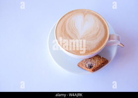 Cappuccino o latte caffè nella tazza con schiuma di latte e biscotti.tazza di caffè con biscotti di mandorle su sfondo bianco, copia dello spazio. Latte con cuore Foto Stock