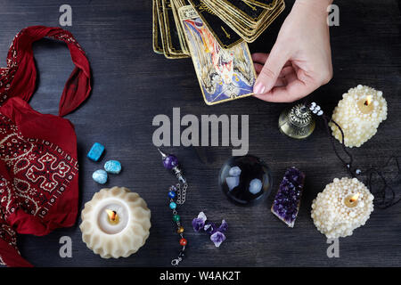 Indovino mani femminili e carte dei tarocchi scuro su un tavolo di legno. Concetto di divinazione. Foto Stock
