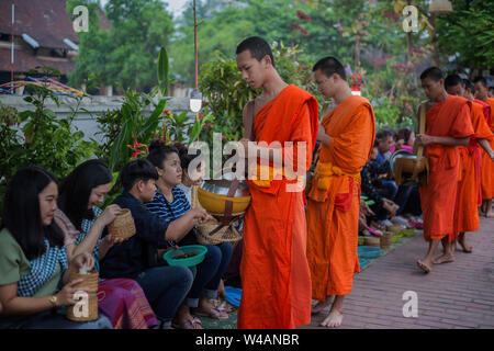 Persone dando elemosina ai giovani monaci buddisti in strada la mattina presto a Luang Prabang, Laos. Il rituale è chiamato Tak Bat. Foto Stock