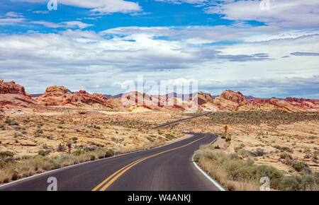 Autostrada nella valle del fuoco Nevada, USA. Svuotare Winding Road passando attraverso il deserto americano e valle rocce rosse, blu cielo nuvoloso sfondo Foto Stock