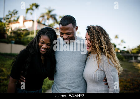 Mescolate la famiglia sorridente e abbracciando sulla spiaggia al tramonto Foto Stock