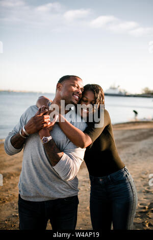 Padre e figlia abbracciando e sorridente sulla spiaggia al tramonto Foto Stock