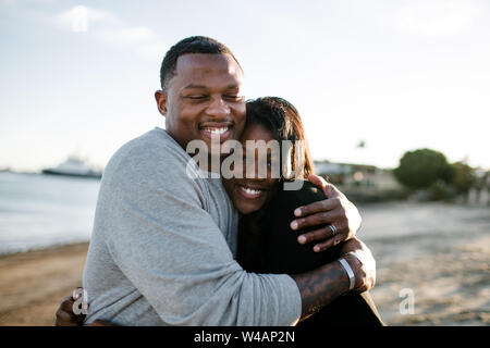 Padre e figlia abbracciando e sorridente sulla spiaggia al tramonto Foto Stock