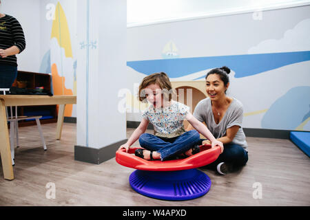 Insegnante sorride mentre lei gira il suo studente su un sedile sensoriali Foto Stock