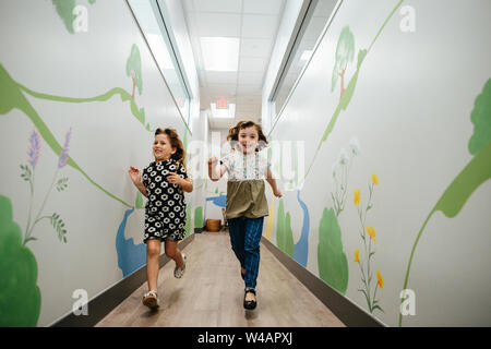 Due ragazze sorriso e scorrere verso il basso un corridoio in un edificio scolastico Foto Stock