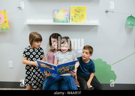 Insegnante e tre studenti di leggere un libro insieme Foto Stock