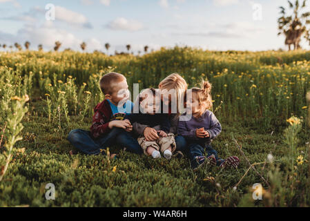 Quattro fratelli sorridente ad ogni altro nel campo di fiori con il blu del cielo Foto Stock