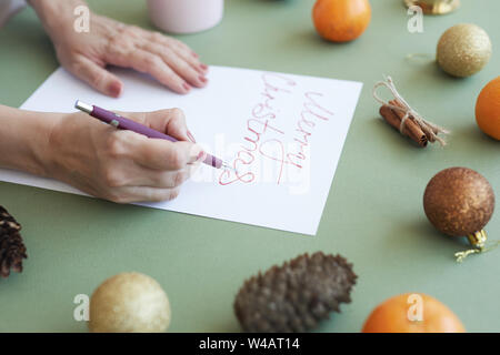 Close-up di un irriconoscibile donna fare lettering per scheda di Natale alla scrivania con decorazioni di vacanza Foto Stock
