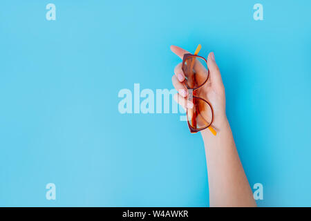 Una femmina mano trattiene delicatamente i bicchieri, schiacciandoli con le dita su uno sfondo blu. Foto Stock