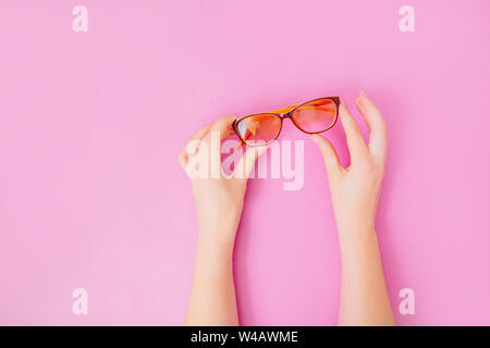 Mani femminili tenendo delicatamente i bicchieri su sfondo rosa. Foto Stock