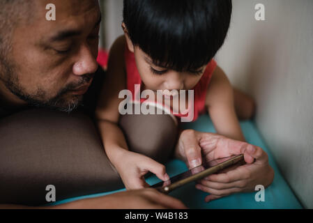 Ragazzo con padre giocare sullo smartphone Foto Stock