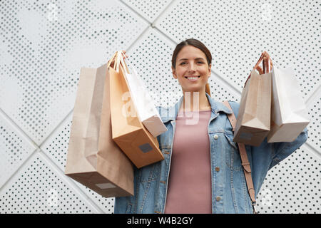 Giovane donna sorridente felice con i nuovi abiti che lei tiene nelle sue mani in varie borse per lo shopping Foto Stock