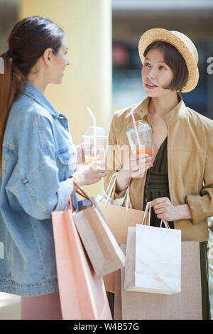 Positivo belle ragazze in abiti casual di bere succo di frutta fresco mentre godendo di pausa durante lo shopping Foto Stock