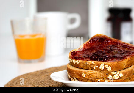 Fette di pane tostato con fatti in casa confettura di fragole per la colazione con sfondo non focalizzato Foto Stock