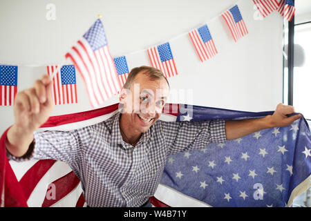 Angolo alto ritratto di balding uomo di mezza età sventolare della bandiera americana e sorridente felicemente in telecamera, spazio di copia Foto Stock