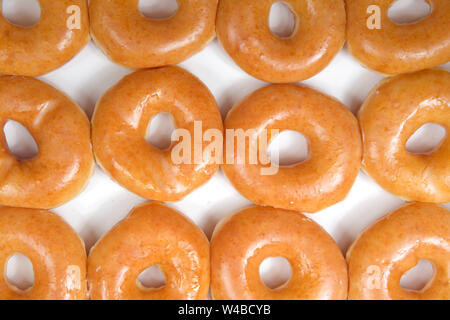 Vista superiore piana vicino laici di pianura ciambelle vetrata in una casella bianca isolata. Una dozzina di ciambelle. L'originale ciambella vetrata è rimasta popoli t preferiti Foto Stock