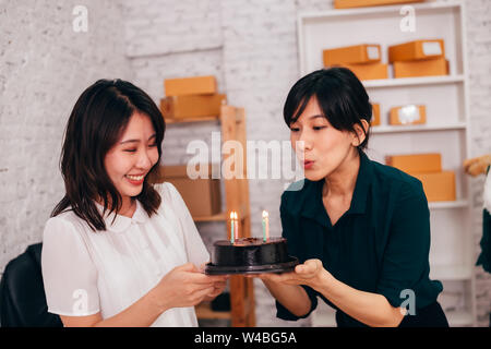 Allegro i colleghi asiatici sorridente e soffiaggio di candele sulla torta mentre festeggia il compleanno in ufficio Foto Stock