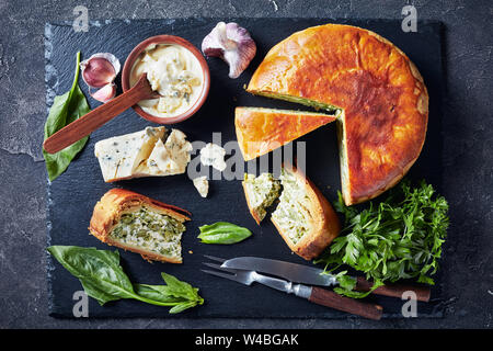 Close-up di spinaci fagiolo verde e blu di formaggio a fette di torta su un nero ardesia vassoio con formaggio blu salsa alla panna in una ciotola su una tavola di cemento, orizzontale Foto Stock