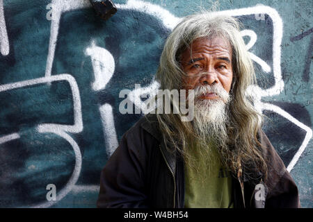 ANTIPOLO City, Filippine - 19 luglio 2019: un anziano uomo filippino con testa grigia e capelli facciali stand contro una parete colorata e pongono per la fotocamera Foto Stock