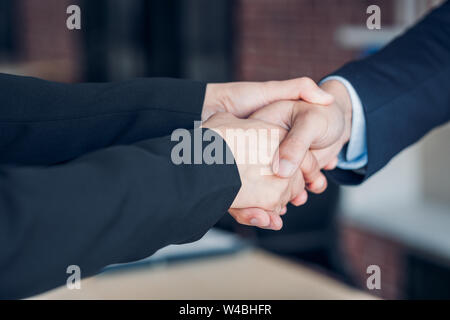 Chiudere fino a due la stretta di mano tra imprenditrice e imprenditore a sala riunioni in ufficio moderno Foto Stock