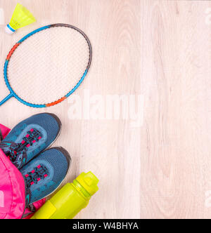 Coppia di blu donna sneakers e bottiglia in rosa zaino, badminton racchetta e volano su bianco superficie in legno Foto Stock