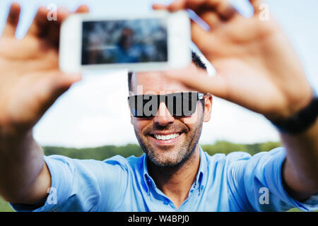 Ritratto di un bel uomo felice prendendo un selfie all'aperto con il suo smartphone Foto Stock